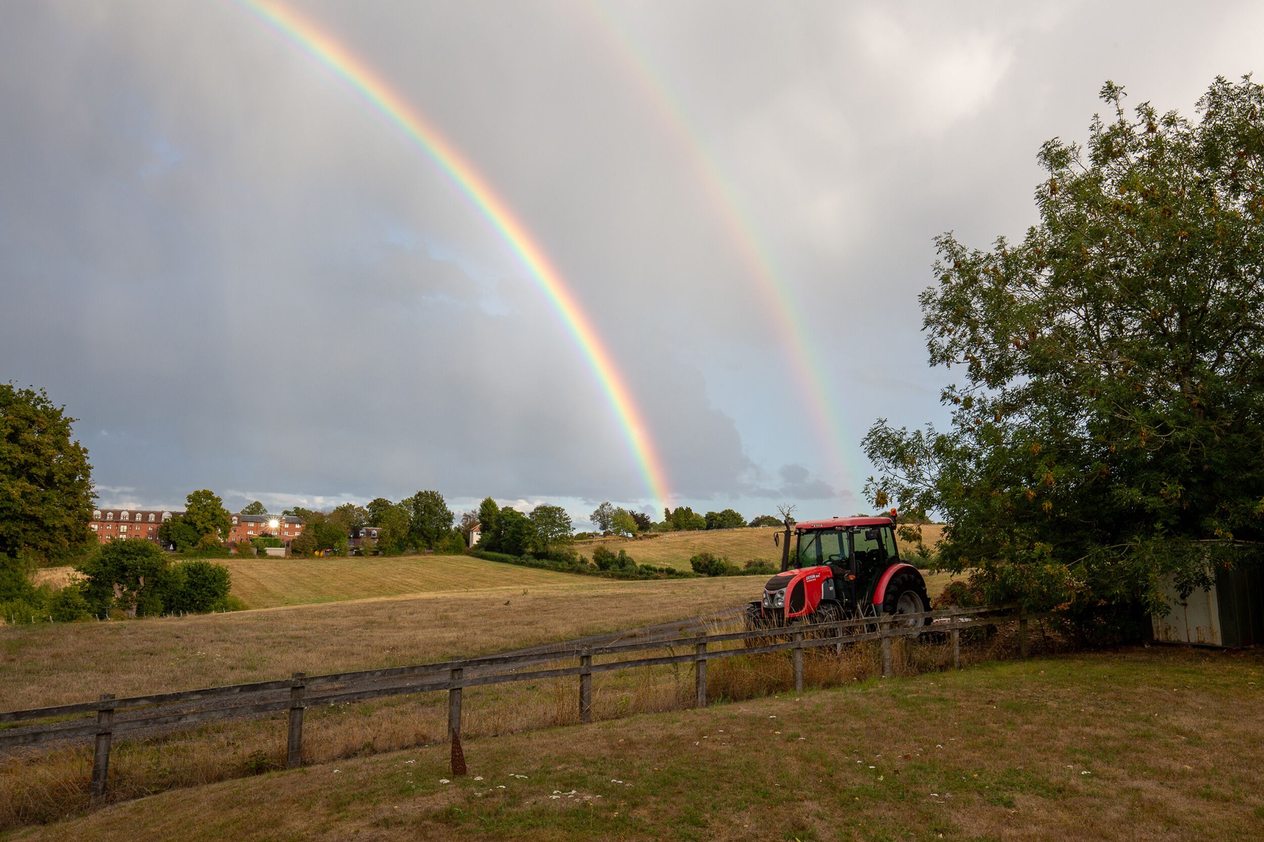Un tracteur rouge dans un champ, avec un arc-en-ciel en arrière-plan.