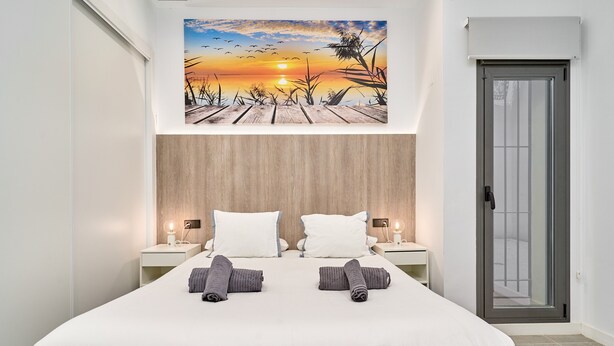 Ein Schlafzimmer mit einem Bett, zwei Nachttischen, einem Sonnenuntergangsbild und einer Tür.