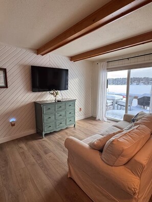Un salon avec un plafond en bois, une commode verte, un canapé beige et un téléviseur fixé au mur.
