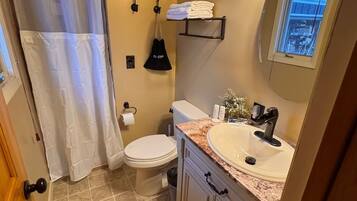 Un baño con inodoro, lavamanos, cortina de ducha, toallero y ventana con vistas.