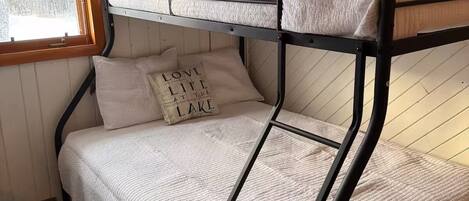 A bunk bed with a window, a pillow with "LOVE LIFE AT THE LAKE" text, and a pillow with "STAY WILD OCEAN CHILD" text.