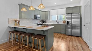 A modern kitchen with a large island, bar stools, stainless steel appliances, and pendant lighting. - Family-Friendly Southside Game House (Chattanooga)