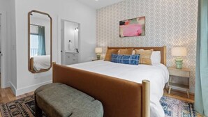 A bedroom with a large bed, a mirror, a bedside table with a lamp, and a patterned wall. - Family-Friendly Southside Game House (Chattanooga)