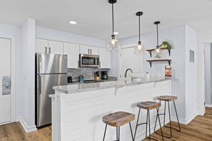 A modern kitchen with white cabinetry, stainless steel appliances, a marble countertop, and hanging pendant lights.