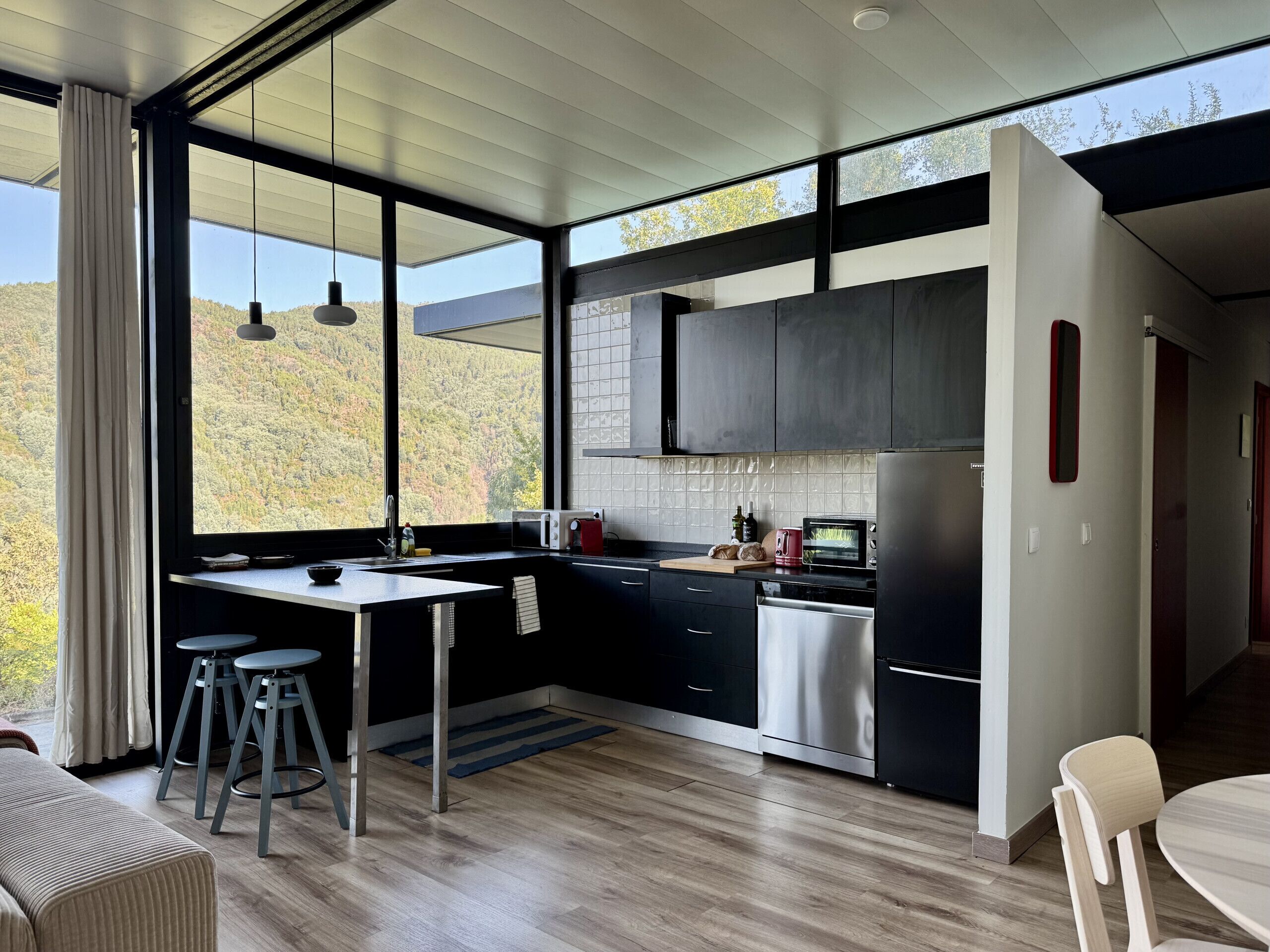 Eine moderne Küche mit großem Fenster, Edelstahlgeräten und einer Essecke mit Hockern.