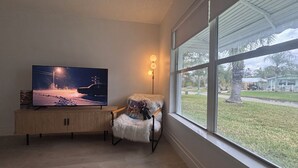 Un salón con un televisor de pantalla plana grande sobre un mueble de madera, un sillón mullido y una lámpara de pie.