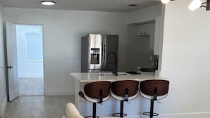 Una sala de estar moderna con un juego de sofá, una zona de cocina con refrigerador y una mesa de comedor con sillas.
