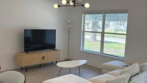 Una sala de estar moderna con un televisor de pantalla plana, un sofá, una mesa de centro y un ventanal con vistas al exterior.