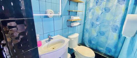 A bathroom with a white sink, toilet, and blue-tiled walls. There are shelves above the toilet and a shower curtain with a floral pattern.