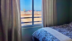 Ein Zimmer mit einem großen Fenster, einem Bett mit gemusterten Betttextilien und Vorhängen.