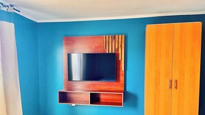 Ein Zimmer mit blauer Wand, einem Holzschrank und einem an der Wand befestigten Fernseher.
