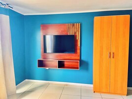 Una habitación con pared azul, un armario de madera y un televisor montado en la pared.