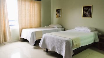 Una habitación de hotel con dos camas individuales, una ventana con cortinas y dos cuadros en la pared.