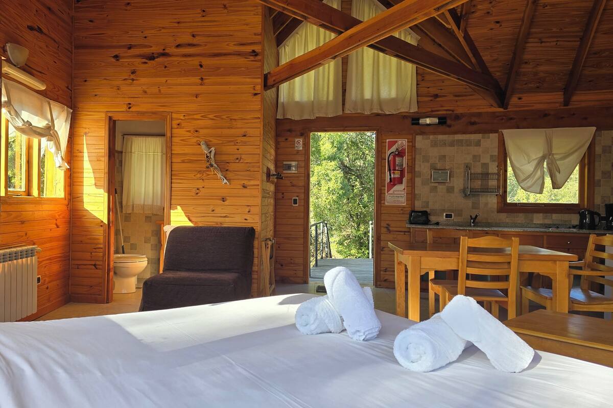 Una cabaña de madera con cama, una silla, una mesa y una pequeña cocina.