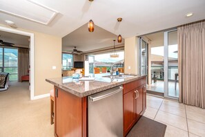A modern kitchen with a granite countertop, stainless steel appliances, and a sliding glass door leading to a balcony. - Honua Kai | Ocean View 7 BR, Sleeps 20 | Car Incl. w/ 6+ Nights | HKH ML-1949 by KBM (Lahaina)
