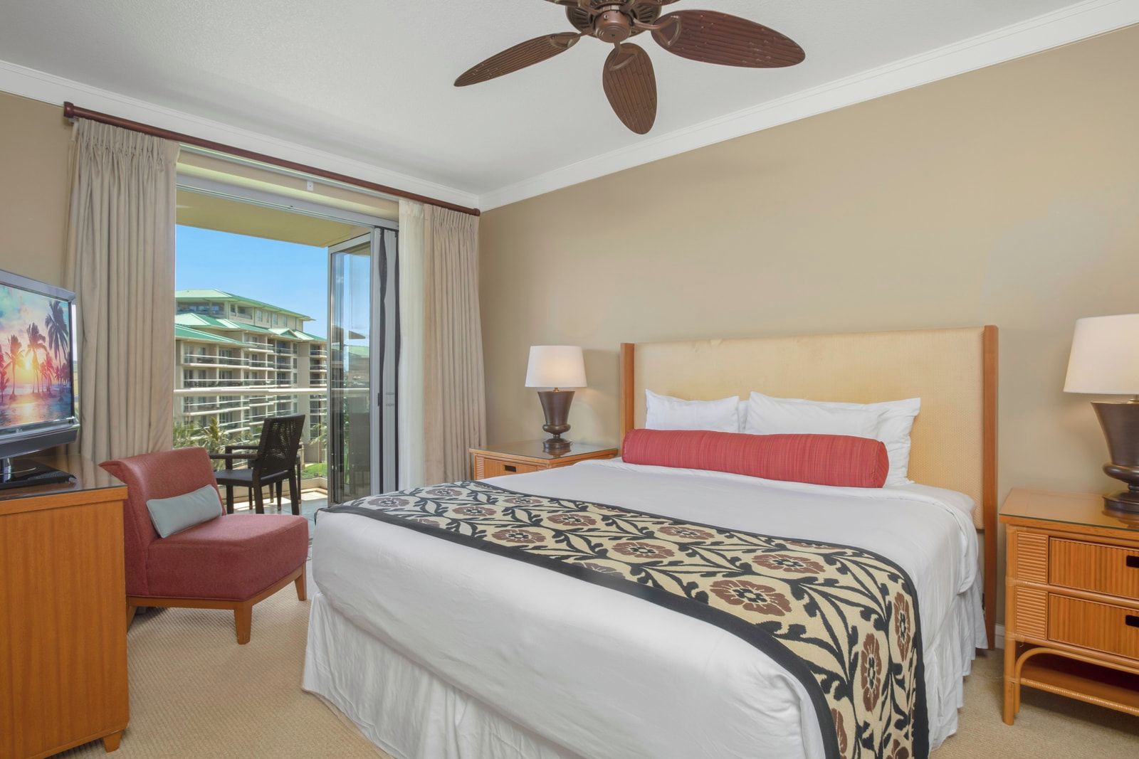 A hotel room with a bed, a desk, a chair, a television, a ceiling fan, and a view of a building through a large window.