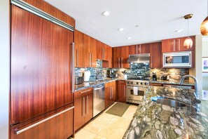 A modern kitchen with wooden cabinets, stainless steel appliances, and a granite countertop. - Honua Kai | Ocean View 7 BR, Sleeps 20 | Car Incl. w/ 6+ Nights | HKH ML-1949 by KBM (Lahaina)