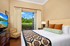 A hotel room with a bed, a TV, a chair, and a view of greenery.
