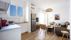 A modern kitchen with white cabinets, a stainless steel refrigerator, and a dining area with wicker chairs and a sofa. - Cozy 2BR Near Metro Acropolis View (Athens)