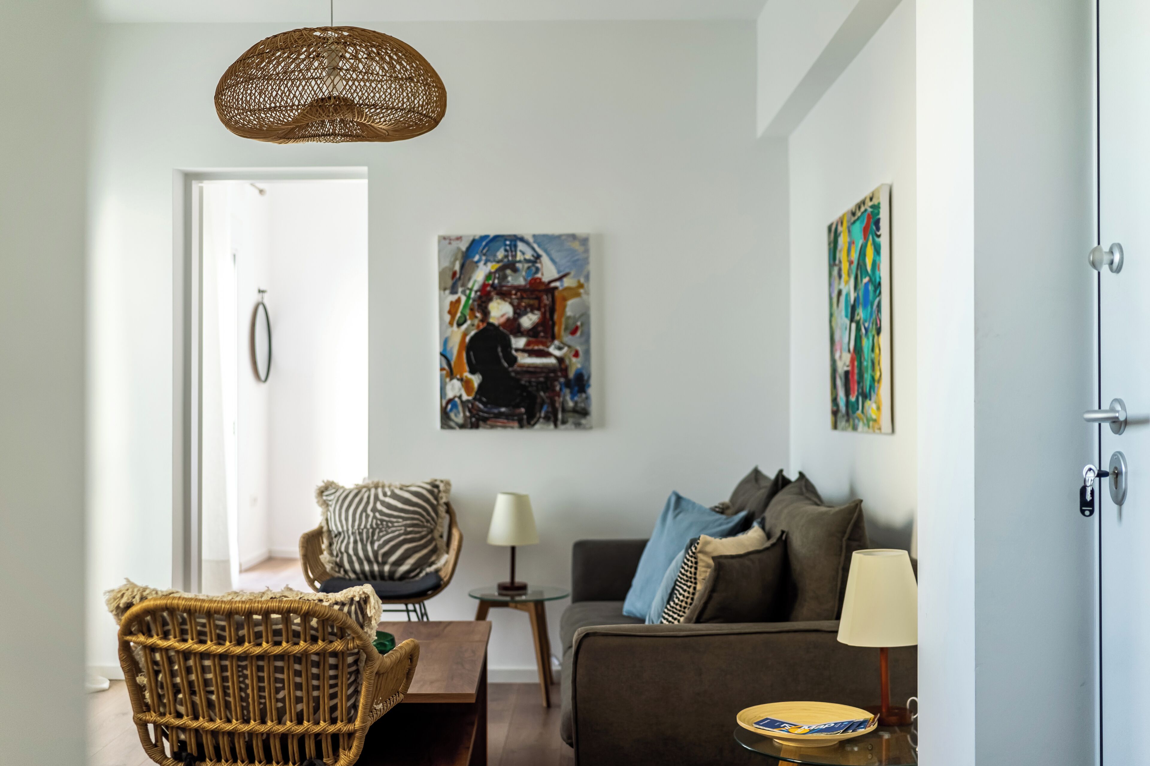 A modern living room with a wicker chair, a sofa, a coffee table, and artwork on the walls.