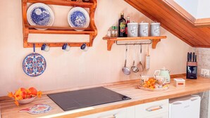 A kitchen with wooden shelves holding plates, mugs, and spices. There is a black induction cooktop, a kettle, and a coffee maker on the counter. - Residenza Marmarole by Ca-Sa Check (Pieve di Cadore)