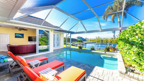 A covered outdoor swimming pool area with lounge chairs, a hot tub, and a view of the surrounding landscape.