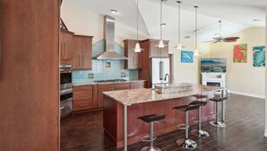 A modern kitchen with wooden cabinets, a central island with bar stools, stainless steel appliances, and pendant lighting.