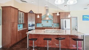 A modern kitchen with wooden cabinets, a central island with bar stools, stainless steel appliances, and pendant lighting.