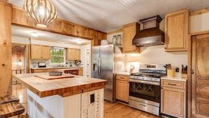 A kitchen with wooden cabinets, a stainless steel refrigerator, a stove, and a large island with a bowl.