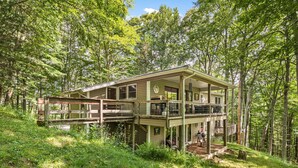 A two-story cabin with a balcony, surrounded by forest.
