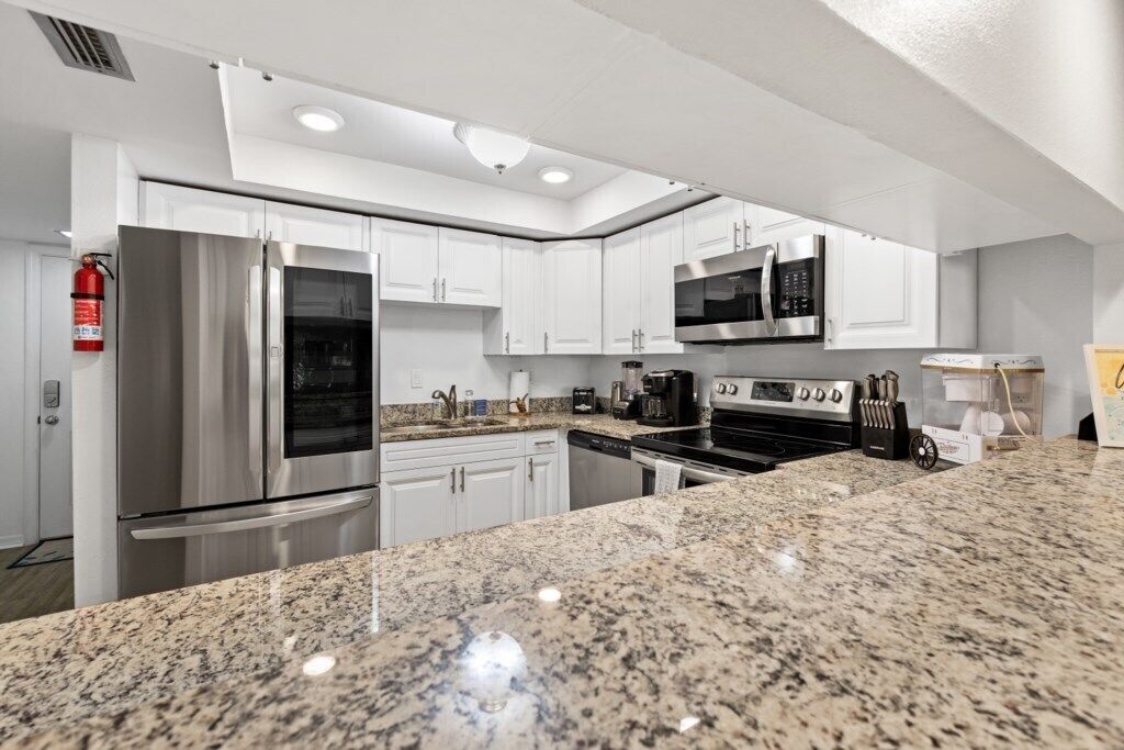 A modern kitchen with white cabinets, stainless steel appliances, granite countertops, and recessed ceiling lights.