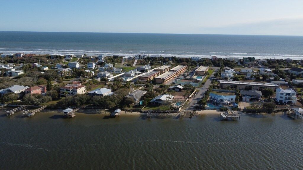 An aerial view of a coastal residential area with houses, a pier, and a beach.