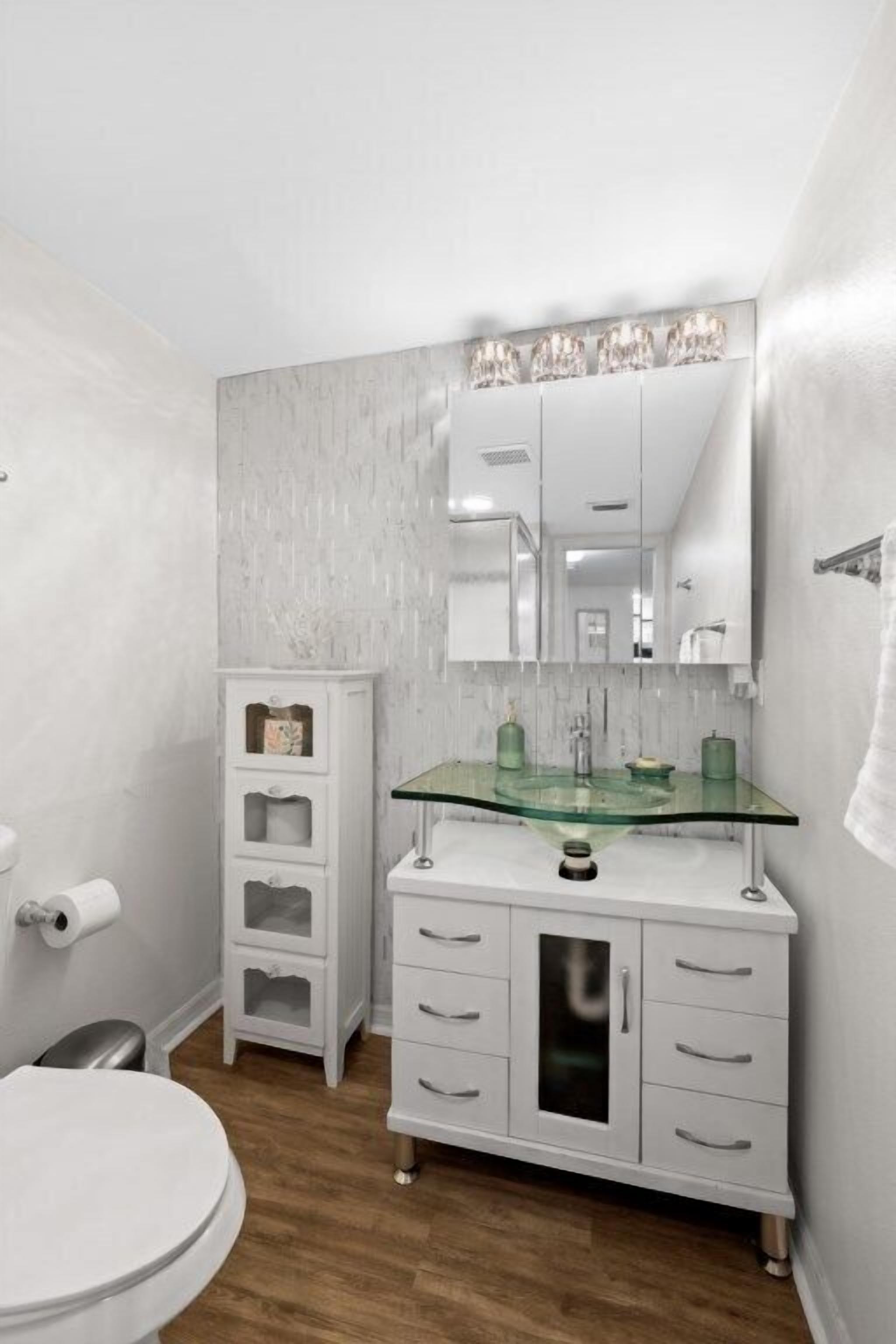 A modern bathroom with a glass sink, white cabinetry, and a large mirror.