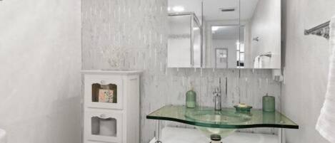 A modern bathroom with a glass sink, white cabinetry, and a large mirror.
