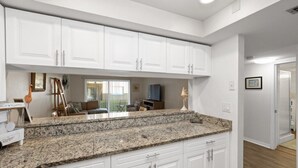 A kitchen with white cabinets, granite countertops, and a view to the dining area. - Pelican Inlet C119 - Near Beach Pool & Tennis (St. Augustine)