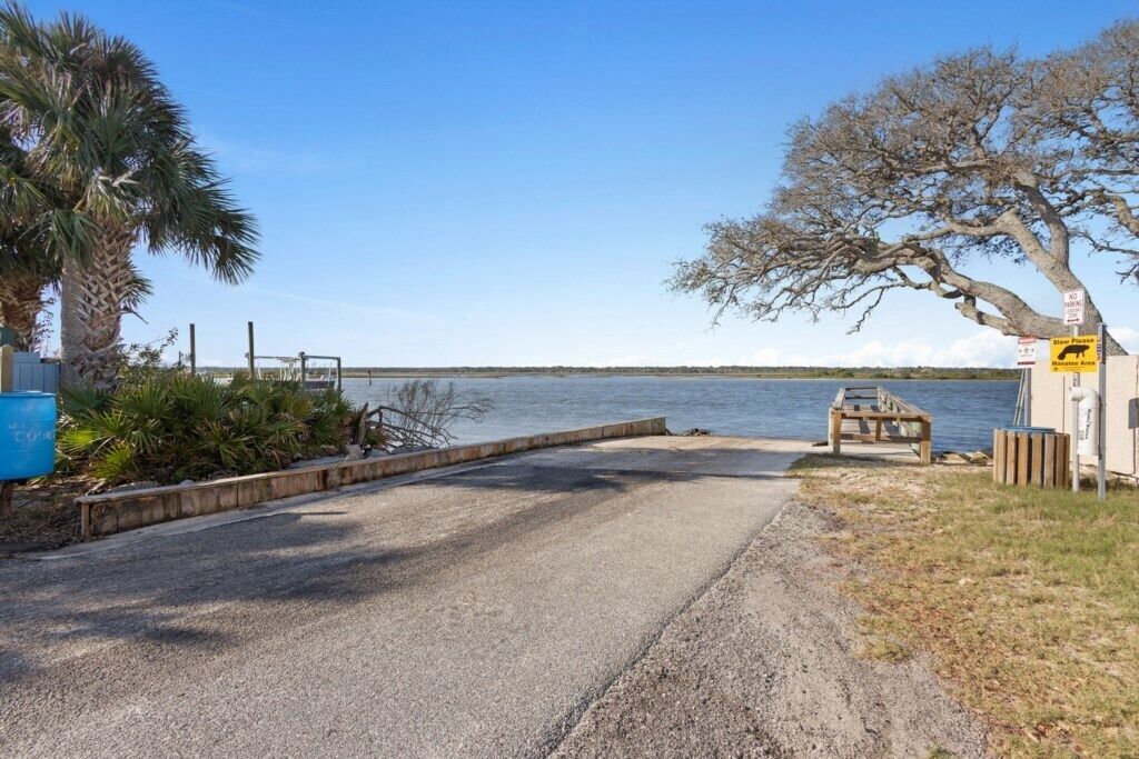 A gravel path leading to a dock by a body of water, with a palm tree and a wooden bench.