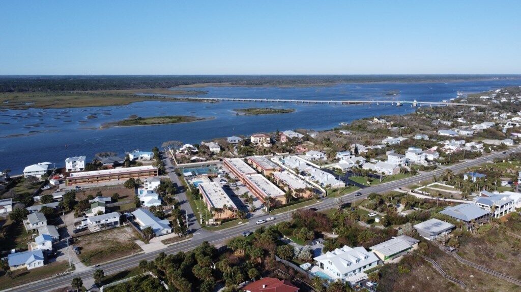 An aerial view of a coastal town with a marina, residential areas, and a bridge in the distance.