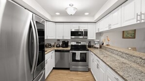 A modern kitchen with stainless steel appliances, white cabinetry, and granite countertops. - Pelican Inlet C119 - Near Beach Pool & Tennis (St. Augustine)