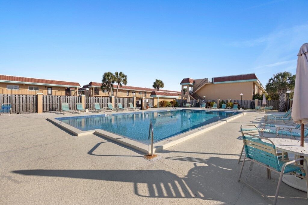 A swimming pool with lounge chairs and umbrellas, surrounded by buildings with a uniform architectural style.