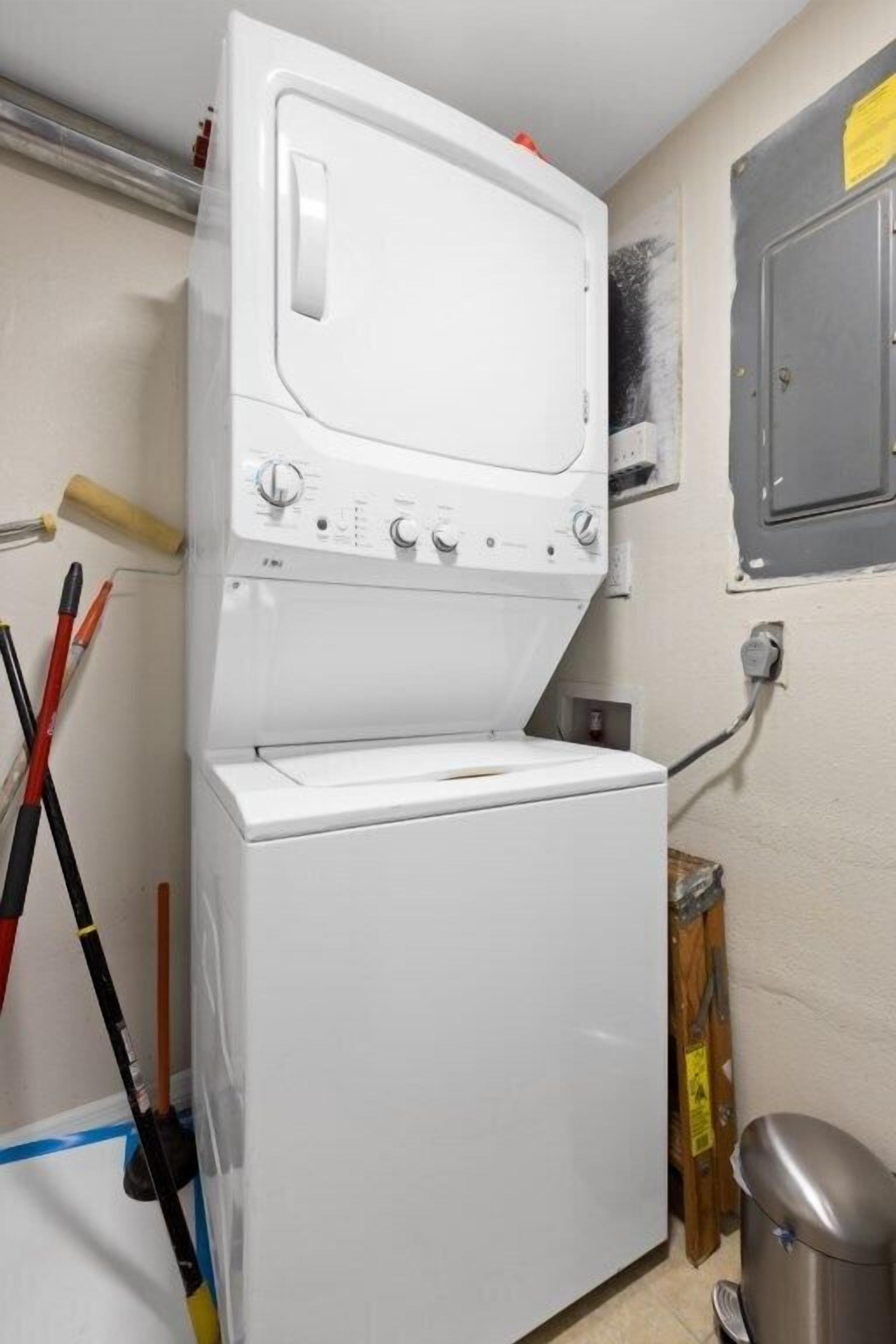 A laundry area with a washing machine and dryer, a wooden floor, and a trash bin.