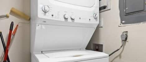 A laundry area with a washing machine and dryer, a wooden floor, and a trash bin.