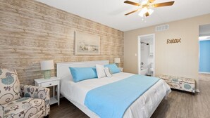 A bedroom with a wooden wall, a bed with blue bedding, a ceiling fan, and a 'Relax' sign on the wall. - Pelican Inlet C119 - Near Beach Pool & Tennis (St. Augustine)