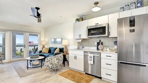 A modern kitchen with a stainless steel refrigerator, microwave, and dishwasher. There is a dining area with a table and chairs, and a view of the outdoors through large windows. - The White House on Flagler Beach - All (Flagler Beach)