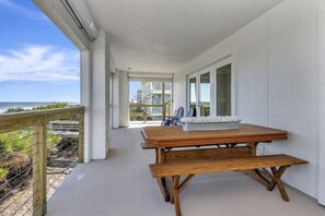 A wooden table and bench on a balcony with a view of the ocean and beach.