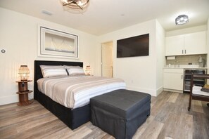 A bedroom with a bed, bedside lamps, a large framed picture, a TV, and a kitchenette. - The White House on Flagler Beach - Unit 11 (Flagler Beach)