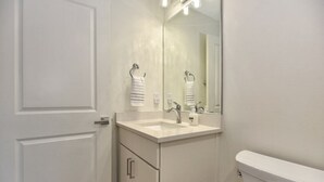 A bathroom with a white sink, a mirror, and a toilet. - The White House on Flagler Beach - Unit 11 (Flagler Beach)