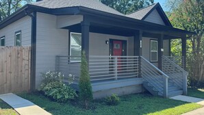 A single-story house with a covered porch, a red door, and a small staircase leading to the entrance.