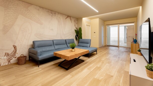 A modern living room with a blue sofa, a wooden coffee table, and a large wall mural. - Miramare by Monholiday (Monopoli)