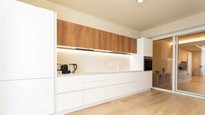 A modern kitchen with white cabinetry, a wooden upper shelf, and a built-in oven. - Miramare by Monholiday (Monopoli)