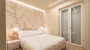 A bedroom with a bed, nightstands, a wall with a floral pattern, and a sliding door with blinds. - Miramare by Monholiday (Monopoli)
